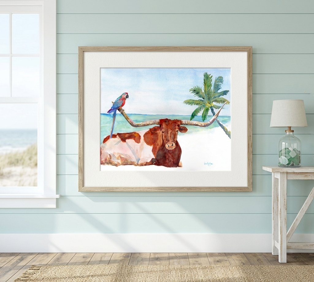  David K Jones’s watercolor painting, Moo-garitaville, framed in a light natural wood frame with a white mat board. The art is displayed on a light seafoam green shiplap wall in a bright, coastal-style room next to a window with an ocean view.