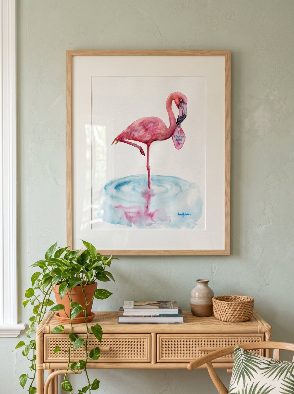 A watercolor painting titled "Flamingo Motel davidkjonesart.jpg", featuring a pink flamingo standing on one leg in a shallow pool of light blue water with its pink reflection visible below. The flamingo is holding a retro pink motel keychain in its beak with the text "Flamingo Motel Room 7". The artwork is signed by the artist in the bottom right corner.