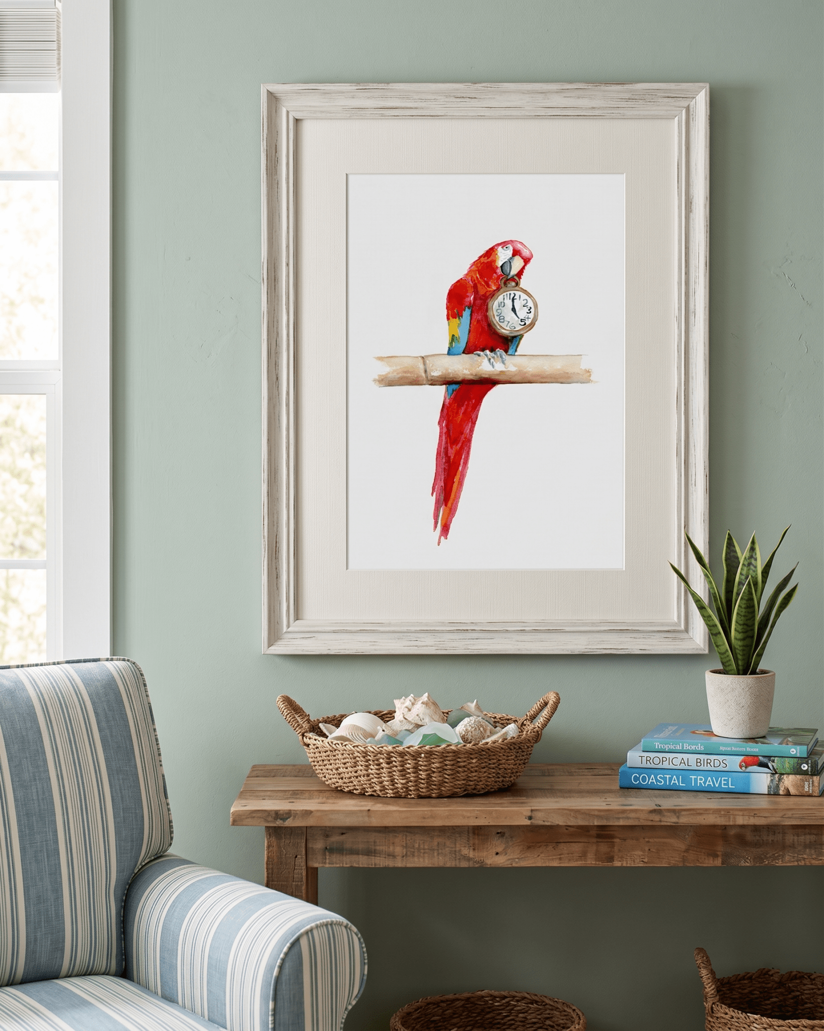 Framed watercolor painting by artist David K. Jones titled "It's Five O'clock HERE," featuring a vibrant scarlet macaw parrot perched on a bamboo branch against a clean white background. The red, blue, and yellow parrot holds a vintage pocket watch in its beak, with the hands explicitly pointing exactly to 5:00. Hung on a light green wall over a table with seashells.