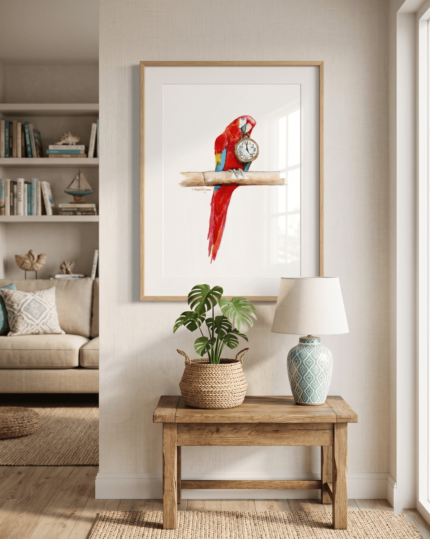 Framed watercolor painting by artist David K. Jones titled "It's Five O'clock HERE," featuring a vibrant scarlet macaw parrot perched on a bamboo branch against a clean white background. The red, blue, and yellow parrot holds a vintage pocket watch in its beak, with the hands explicitly pointing exactly to 5:00. Hung on a white wall over a table with a tropical plant.
