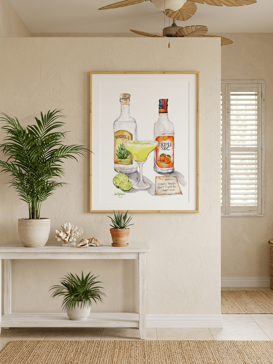 David K. Jones watercolor painting of a margarita cocktail with tequila and Triple Sec bottles. A lime wedge and a handwritten recipe card are also included. The artwork is framed and displayed on a wall, with a white console table and tropical plants in the foreground.