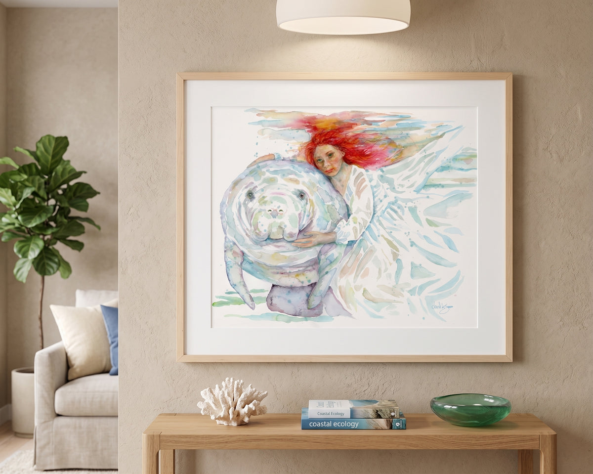 "Mermaids" watercolor painting by David K. Jones, depicting a woman with flowing red hair in a white dress gently embracing a manatee underwater. displayed on a beige wall above a wooden console table in a modern living room setting.