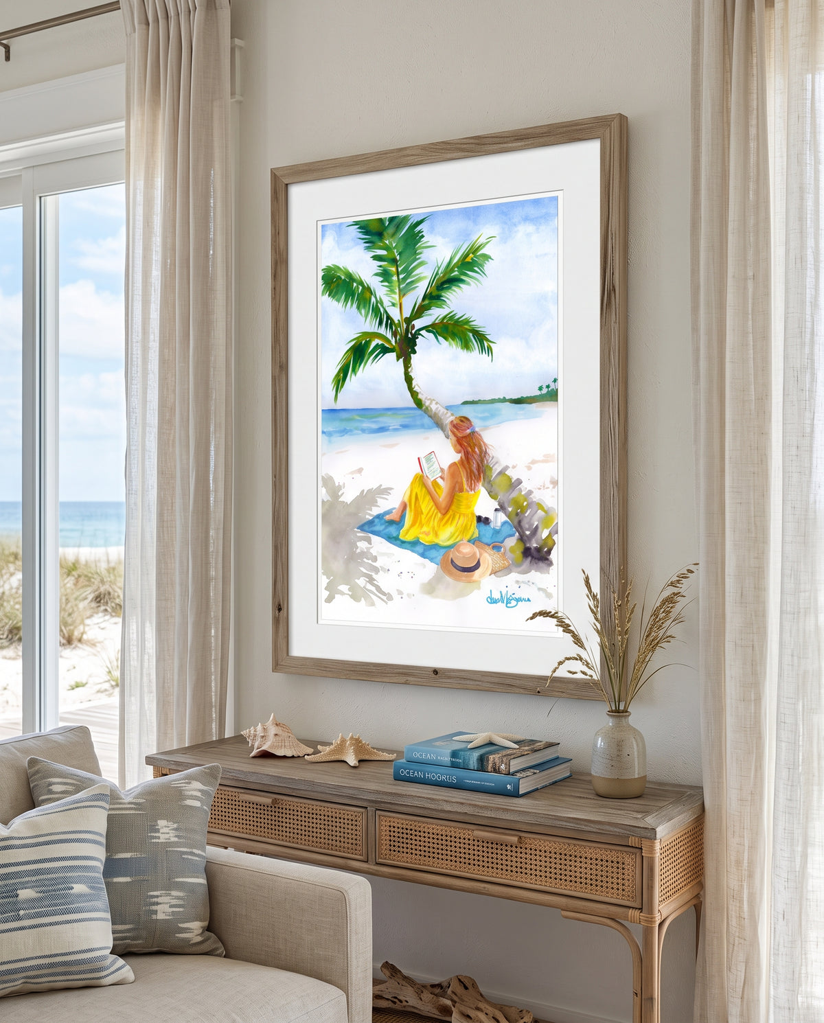 "Turning Pages in Paradise" by David K. Jones. A watercolor painting depicting a woman reading a book on a tropical beach. She wears a bright yellow dress and sits on a blue towel beneath a curved palm tree with green fronds. A straw hat with a black band, sunglasses, a tumbler, and a woven tote bag rest on the white sand nearby, with blue ocean water in the background.The artwork depicts a woman in a yellow dress sitting on a beach towel under a palm tree near the ocean.